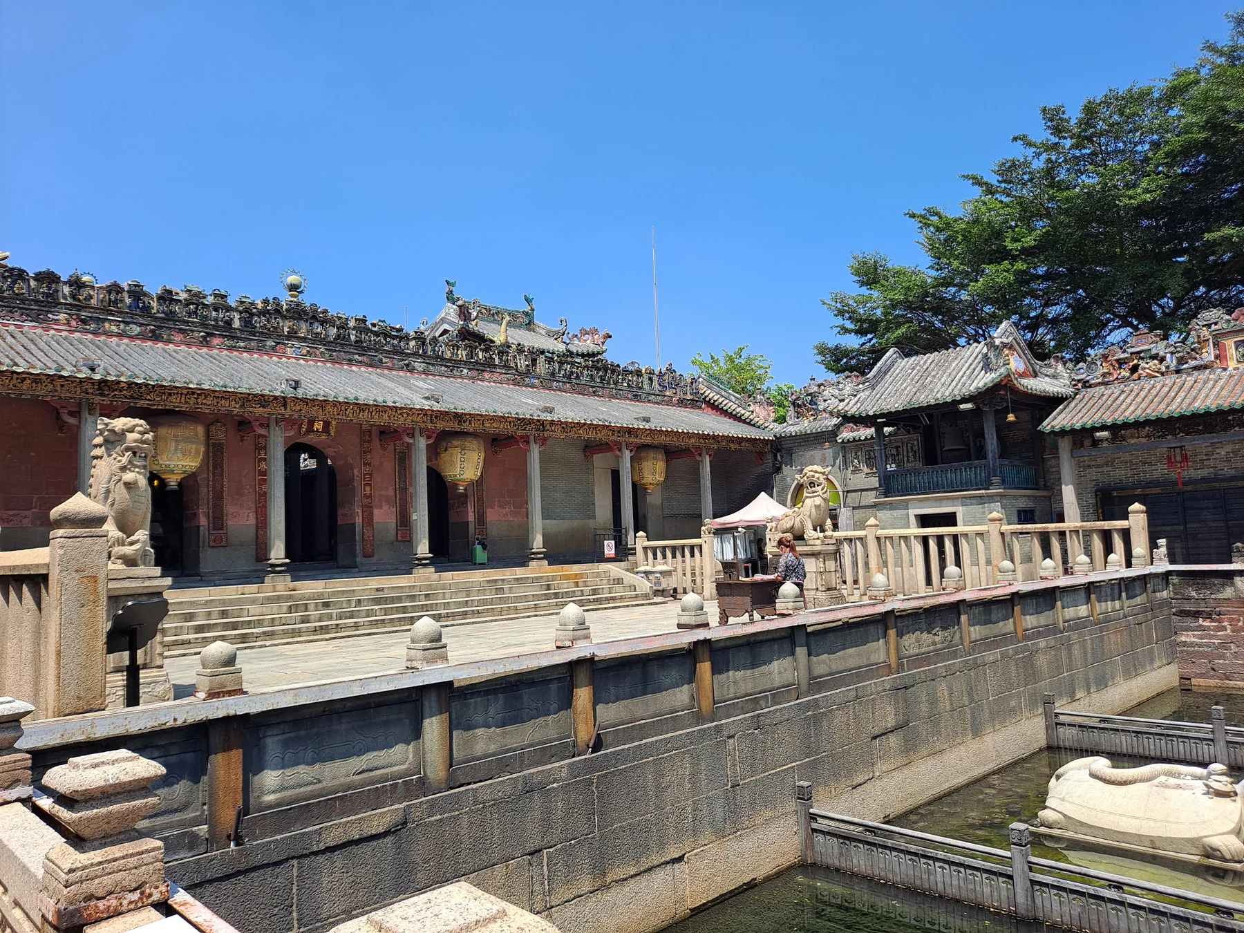 A courtyard view connecting historic halls, roofs, stone railings and water inside Foshan Ancestral Temple